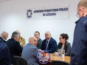Zdjęcia przedstawiają przebieg odprawy rocznej w auli Komendy Powiatowej Policji w Leżajsku. Na zdjęciach widać umundurowanych funkcjonariuszy oraz osoby cywilne - zaproszonych gości, przedstawicieli samorządów powiatu leżajskiego. Zdjęcia wykonane są wewnątrz budynku.
