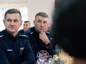Zdjęcia przedstawiają przebieg odprawy rocznej w auli Komendy Powiatowej Policji w Leżajsku. Na zdjęciach widać umundurowanych funkcjonariuszy oraz osoby cywilne - zaproszonych gości, przedstawicieli samorządów powiatu leżajskiego. Zdjęcia wykonane są wewnątrz budynku.