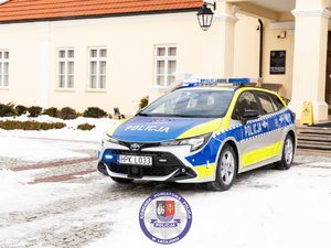 Zdjęci przedstawia oznakowany radiowóz policji. Dookoła jest śnieg. Samochód ma włączone niebieskie sygnały błyskowe.