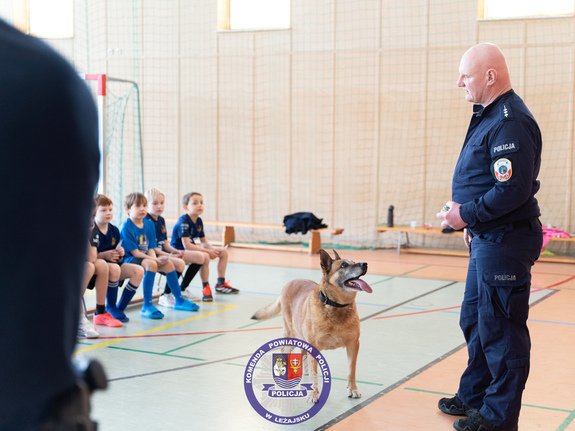 Zdjęcia przedstawiają przebieg spotkania profilaktycznego, w którym udział wzięli umundurowani policjanci z leżajska i podopieczni Akademii Piłkarskiej Pogoni Leżajsk. Na zdjęciach widoczny jest również pies służbowy "Dżina".