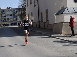 Zdjęcie przedstawia biegnącego po ulicy mężczyznę. Ubrany jest w strój sportowy.