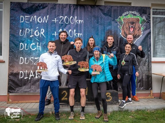 Zdjęcie przedstawia podium na którym stoją zwycięzcy biegu Duch Pogórza. Wśród nich znajduje się Bartosz Ceberak. Osoby ubrane w sportowy ubiór.